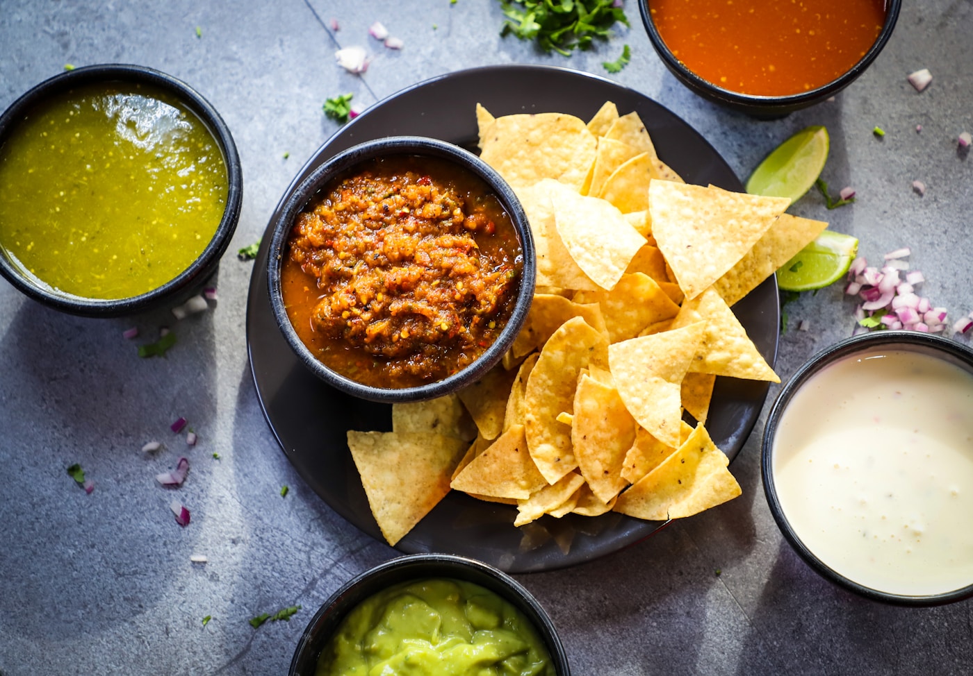 Tortilla chips surrounded by salsa verde, salsa roja, guacamole, and queso dip
