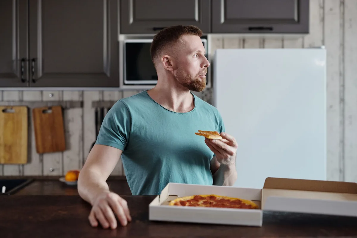 A man eating reheated pizza in a modern kitchen