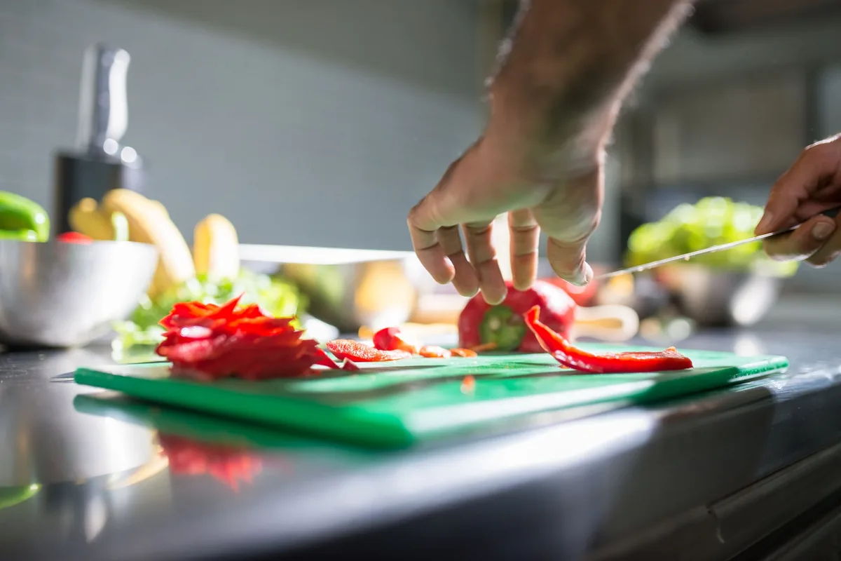Hands slicing a red bell pepper on a chopping board