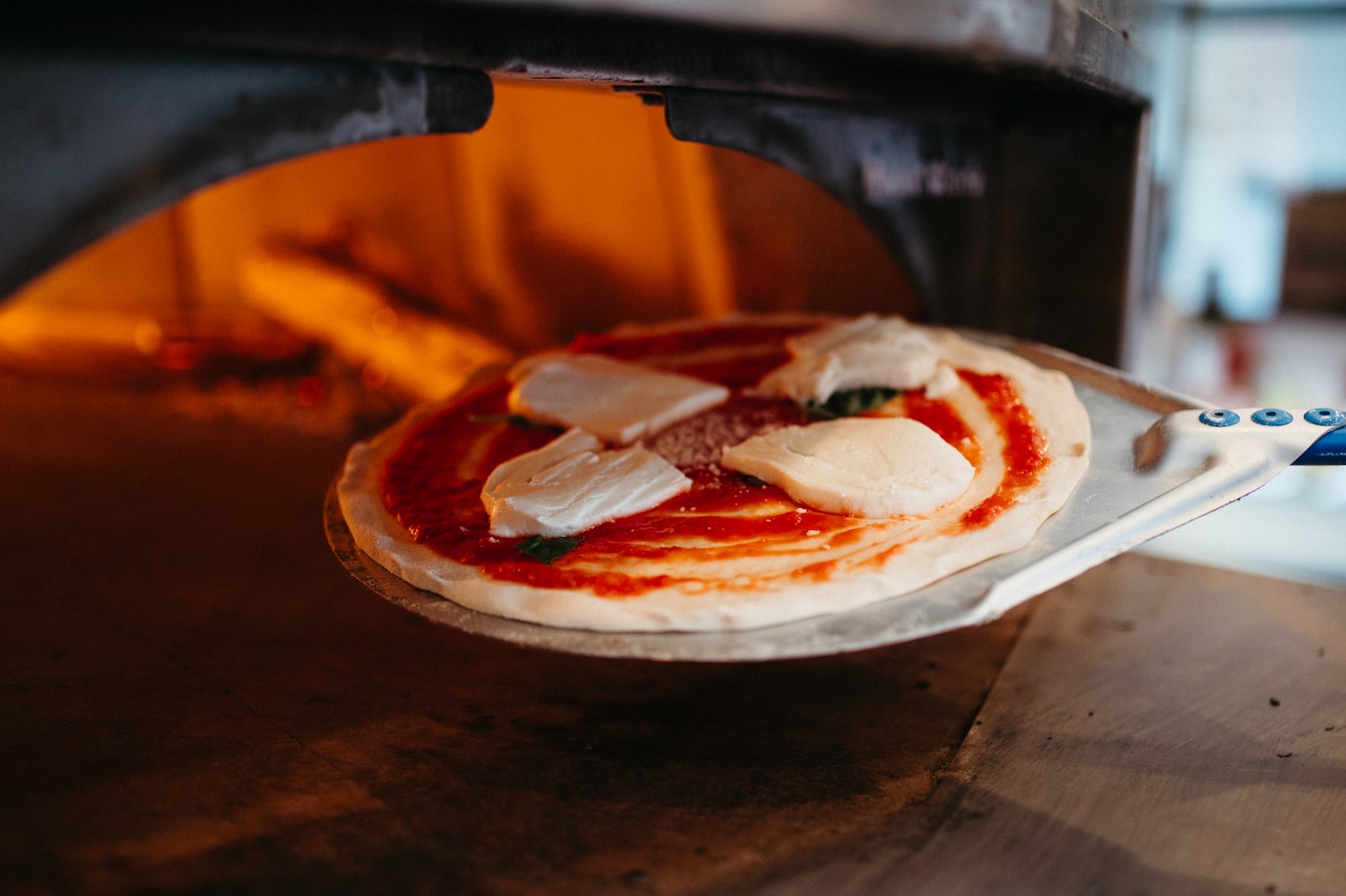 Uncooked pizza being slid into a hot oven on a pizza peel