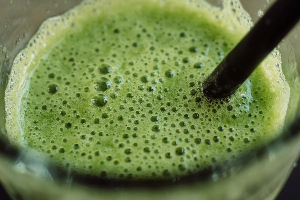 A frothy green smoothie in a glass with a straw