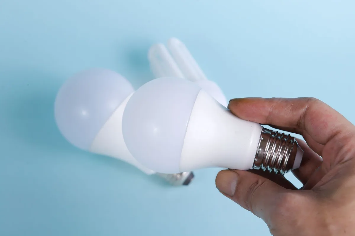 Hand holding a light bulb up to a ceiling fitting