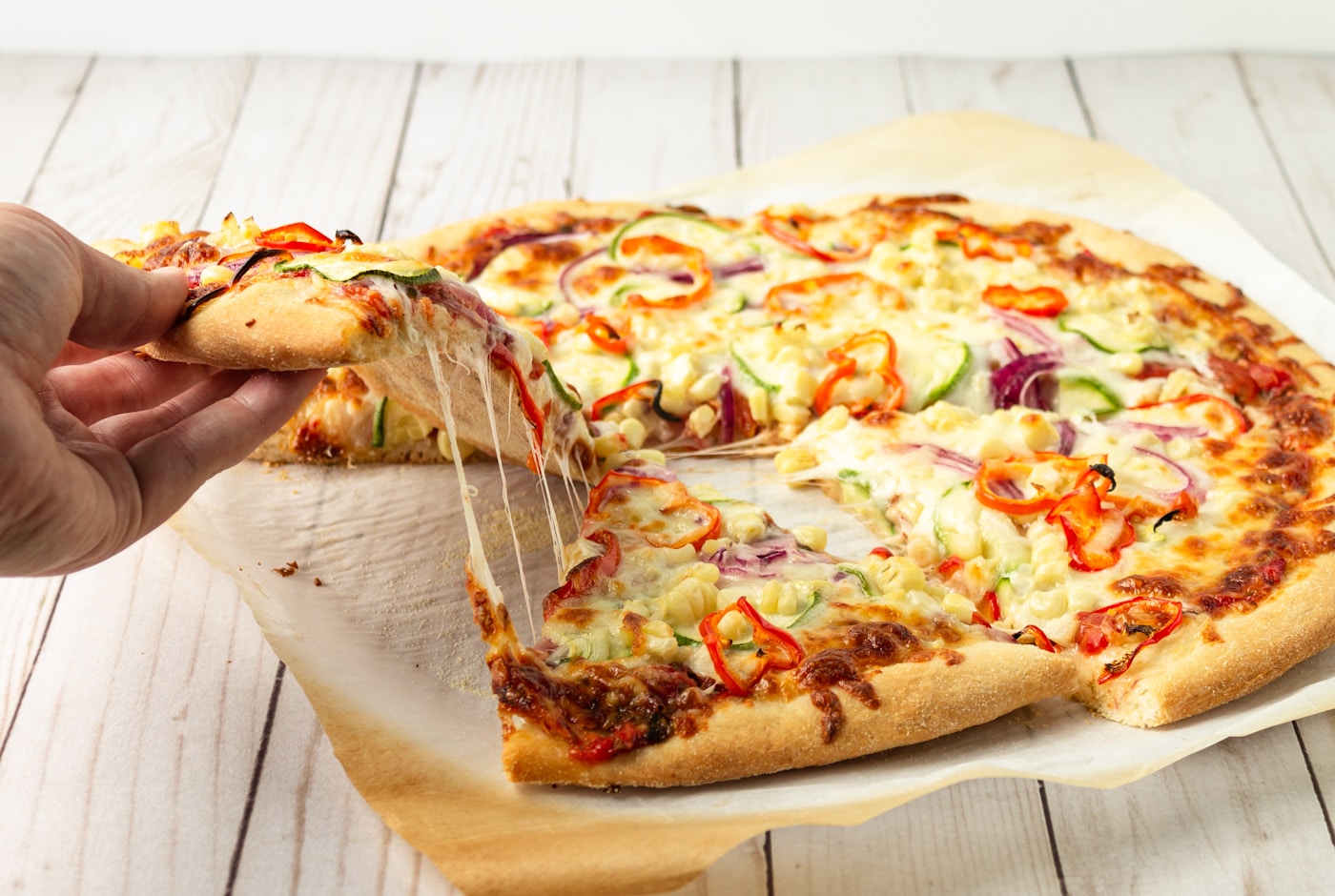 Hand lifting a slice of pizza with melted cheese stretching from the pie