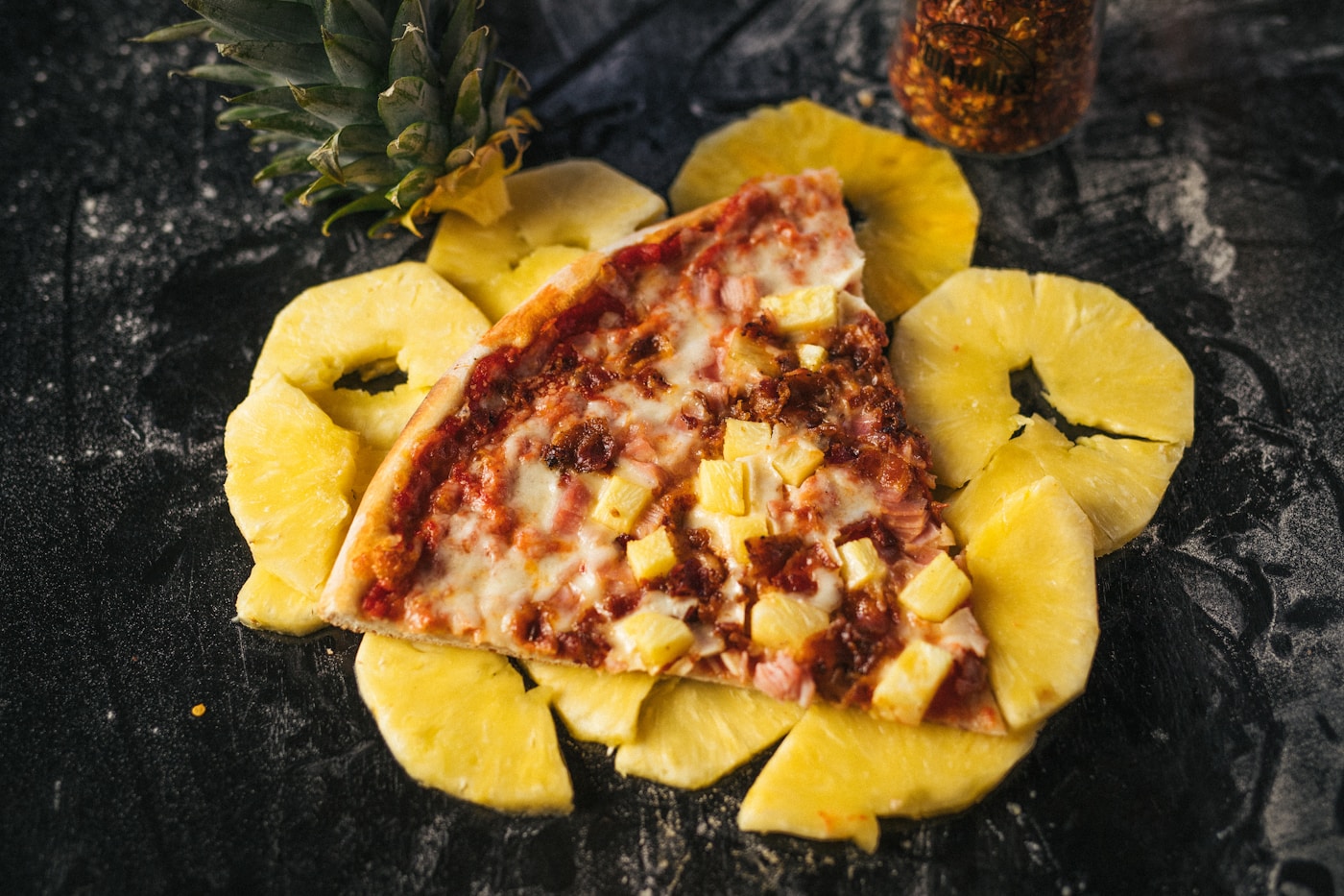 Slice of Hawaiian pizza with ham surrounded by fresh pineapple rings
