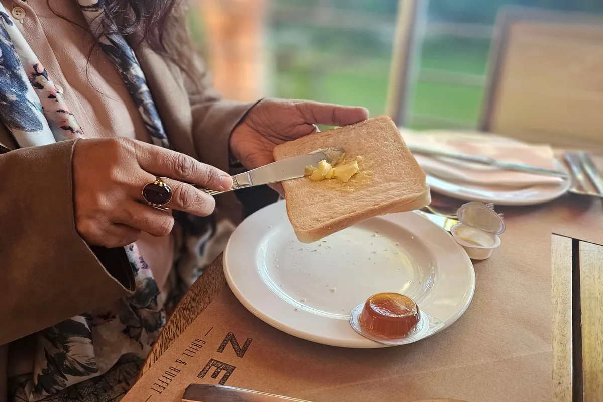 Person spreading butter on toast at a sunny table