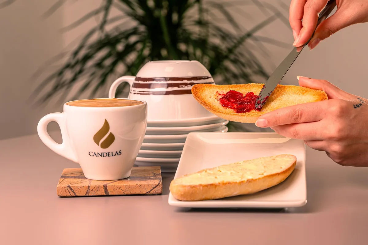 Hand spreading jam on toast with a coffee cup