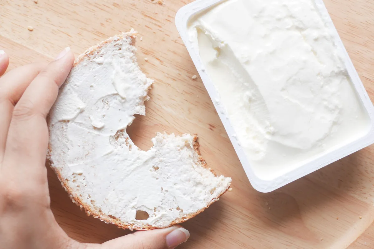 Hand holding a bagel with cream cheese spread