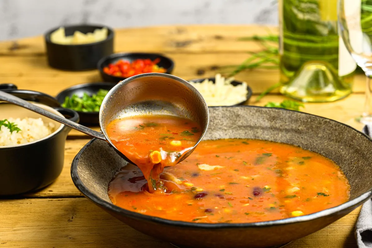 Ladle serving vegetable soup from a rustic bowl