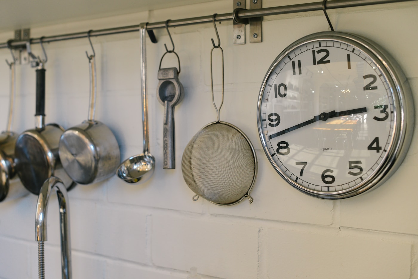 Analog clock hanging on a kitchen wall near cookware