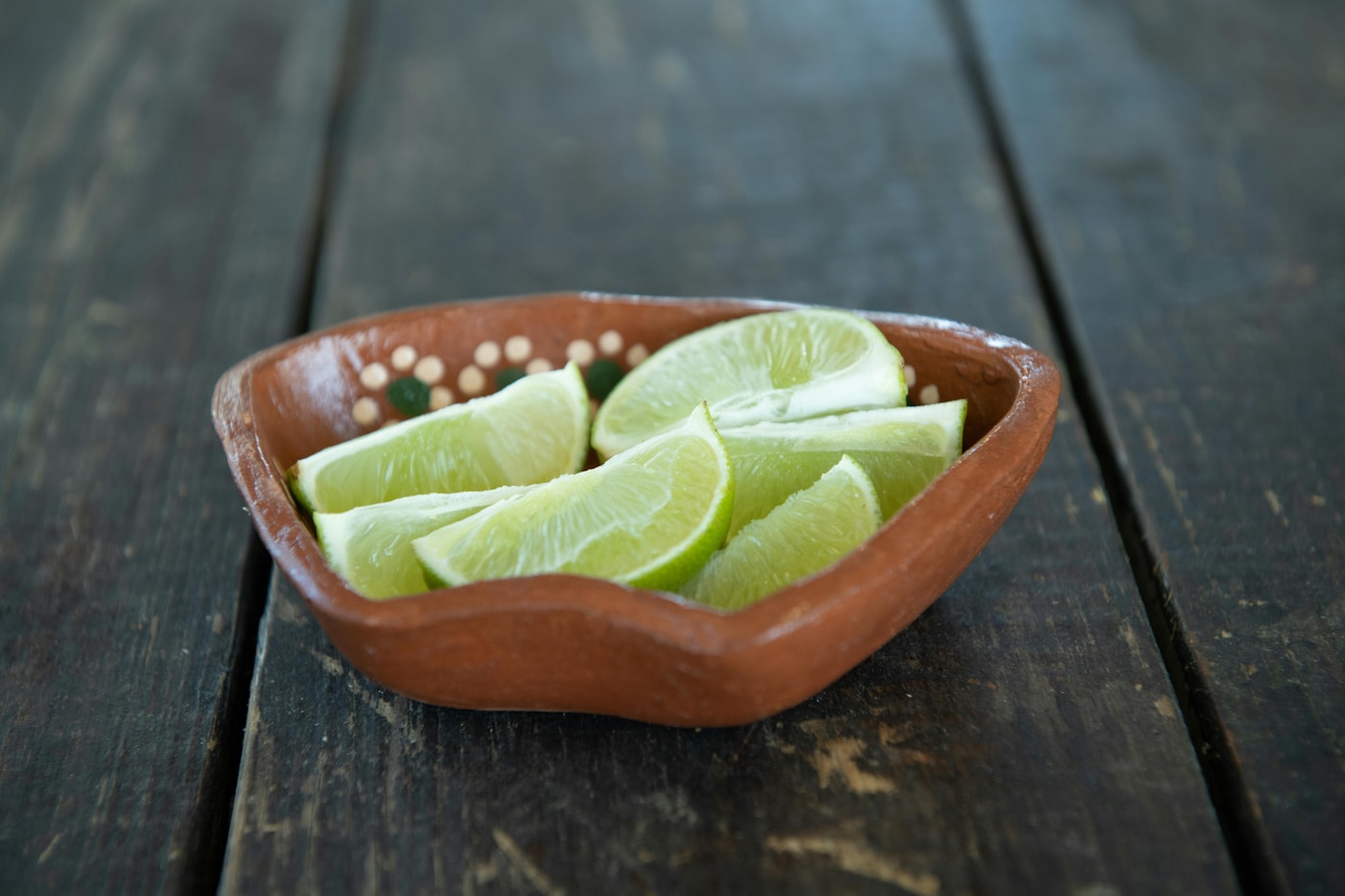 Fresh lime wedges in a small clay bowl on a wooden table