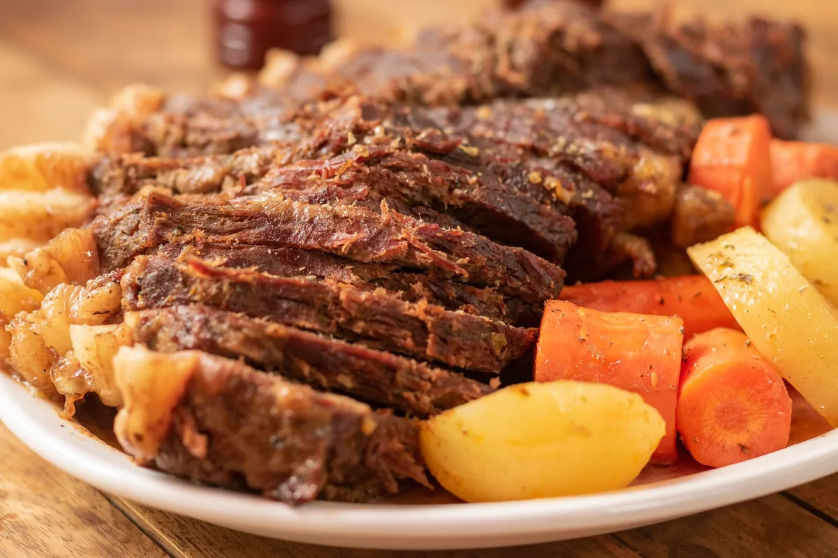 Tender pot roast served with carrots and potatoes on a white plate