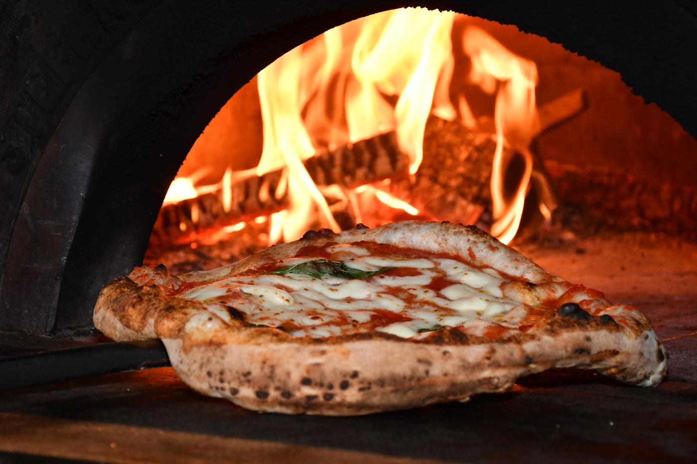 Neapolitan pizza with fresh mozzarella going into a wood-fired oven with visible flames