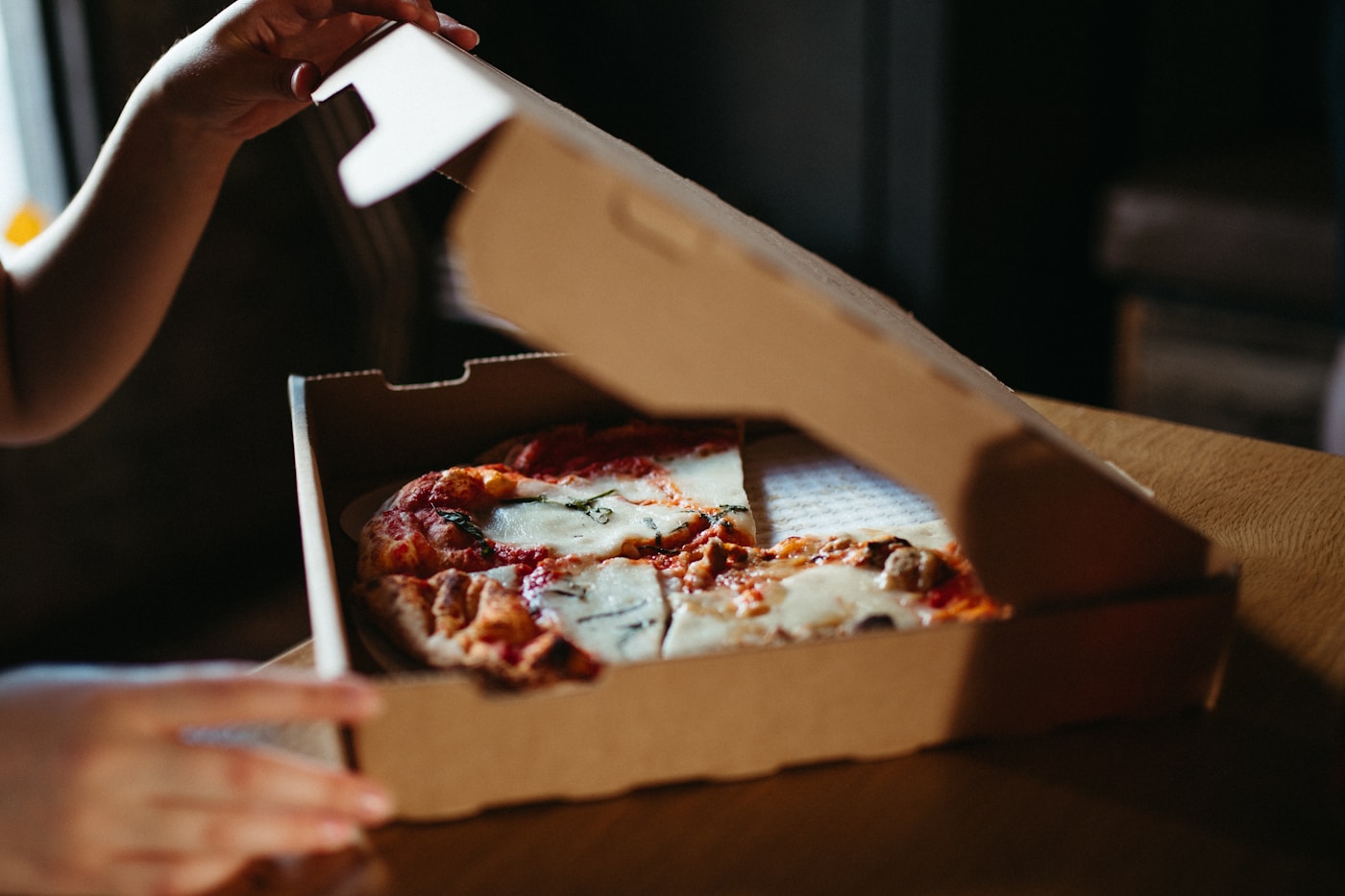 Hands opening a pizza box to reveal a fresh hot pizza inside