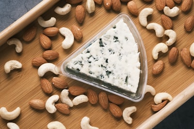 Wedge of blue cheese surrounded by nuts on a wooden board