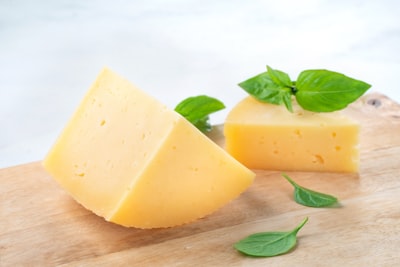 Wedge of cheese with fresh basil on a wooden board