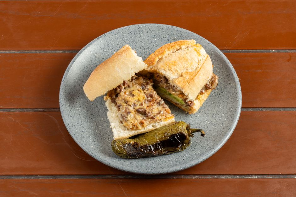Cheesesteak sandwich cut in half on a plate with a grilled pepper