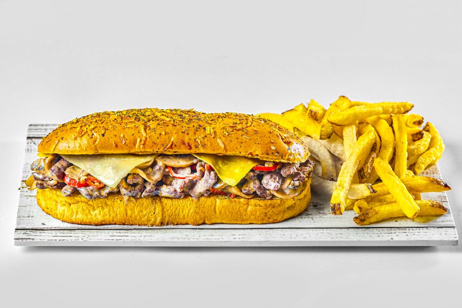 Cheesesteak sandwich served with french fries on a white board