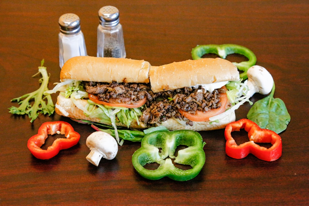 Cheesesteak sandwich surrounded by fresh peppers and mushrooms