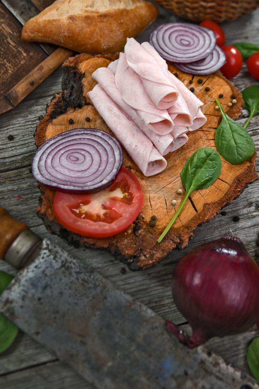 Sliced ham, onions, and tomatoes on a wooden board