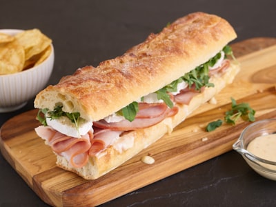 Loaded hoagie sandwich with ham, cheese, and arugula on a wooden board