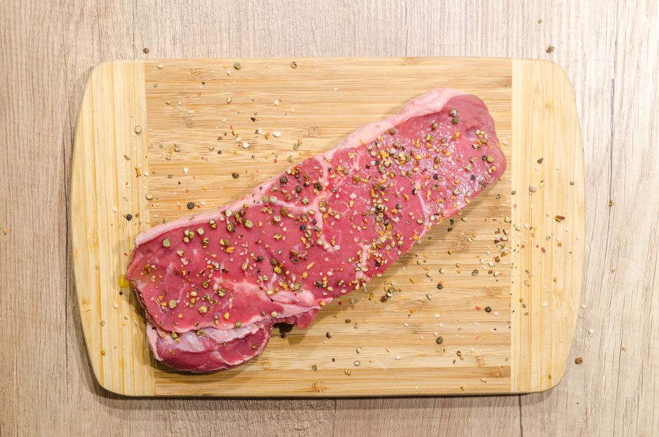 Raw beef steak seasoned with spices on a wooden cutting board
