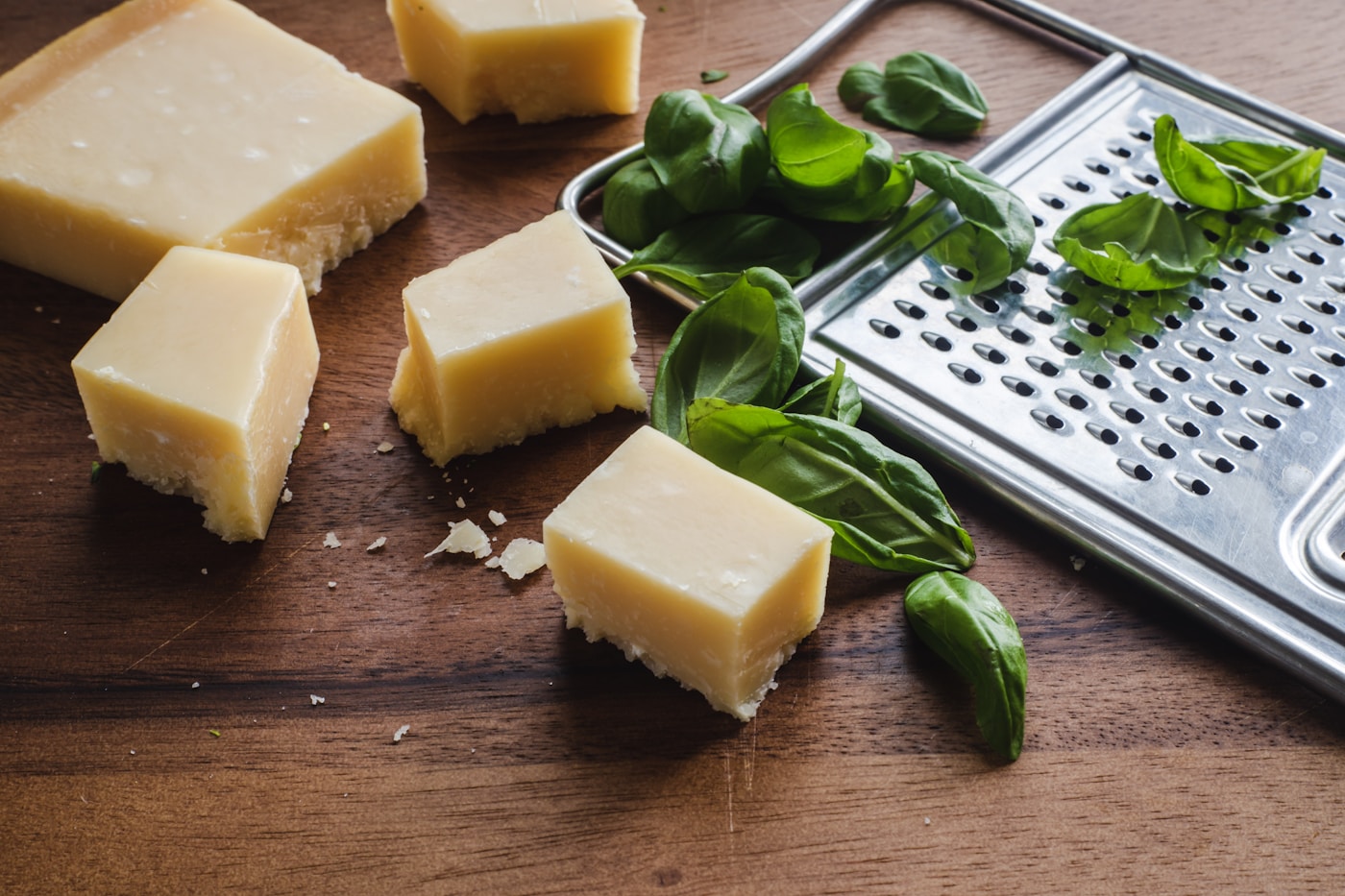 Blocks of hard cheese with fresh basil and a metal grater