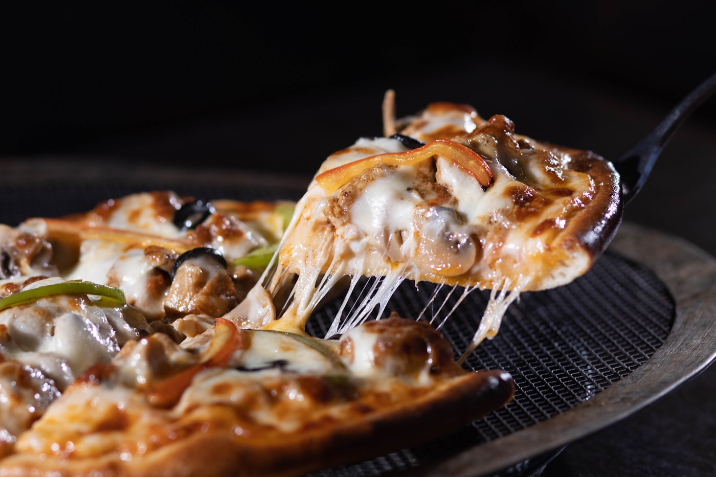 Crispy reheated pizza slice with a cheese pull being lifted with a spatula