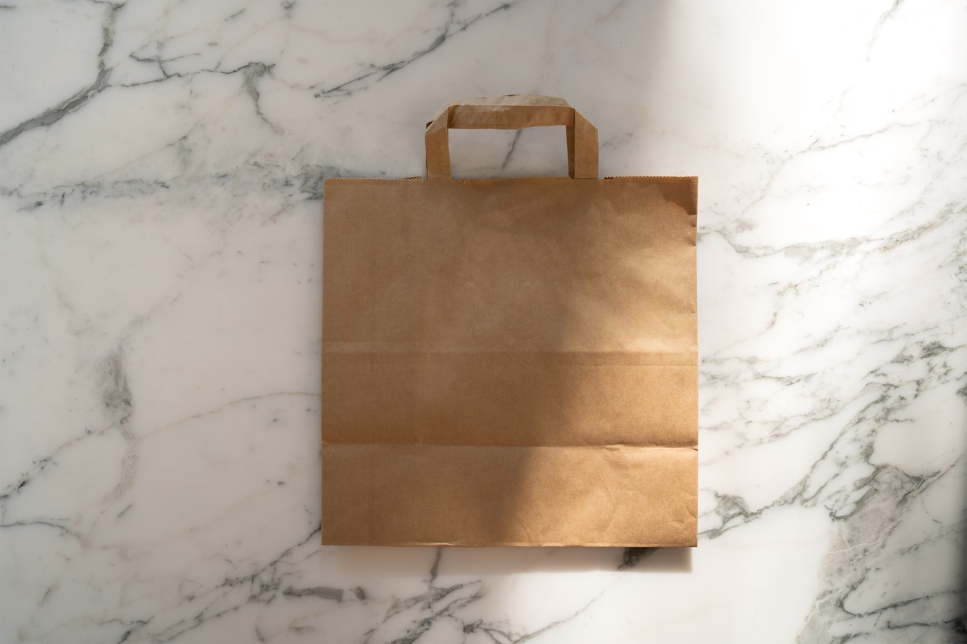 Plain brown paper takeout bag with handles on a marble counter