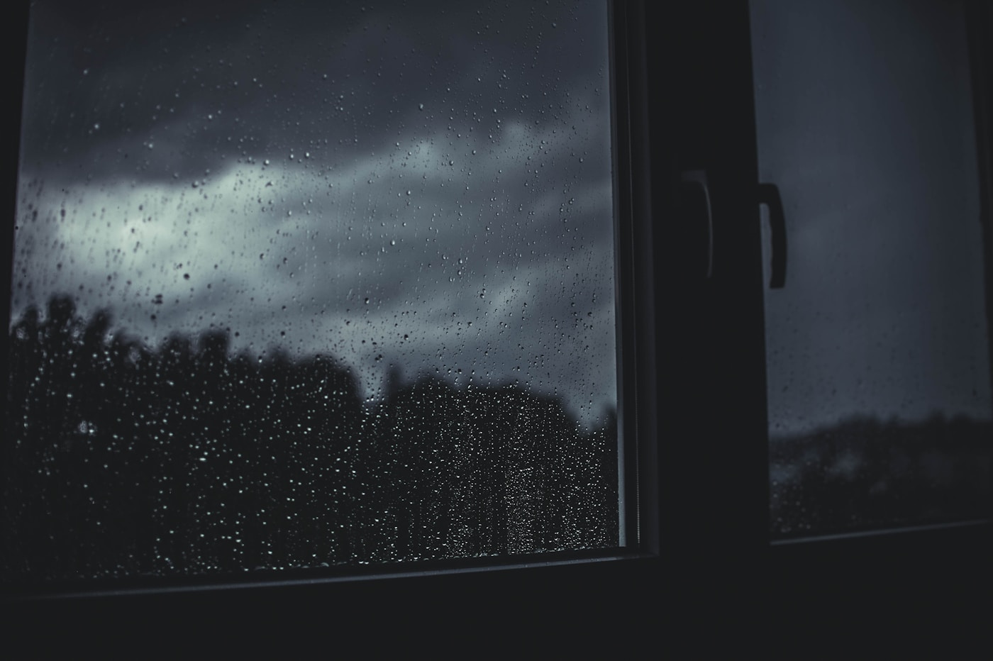Rain drops covering a window with a stormy sky visible outside