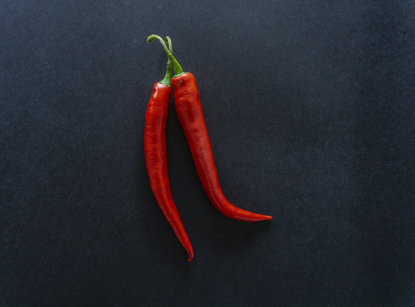 Two whole red chili peppers on a dark surface