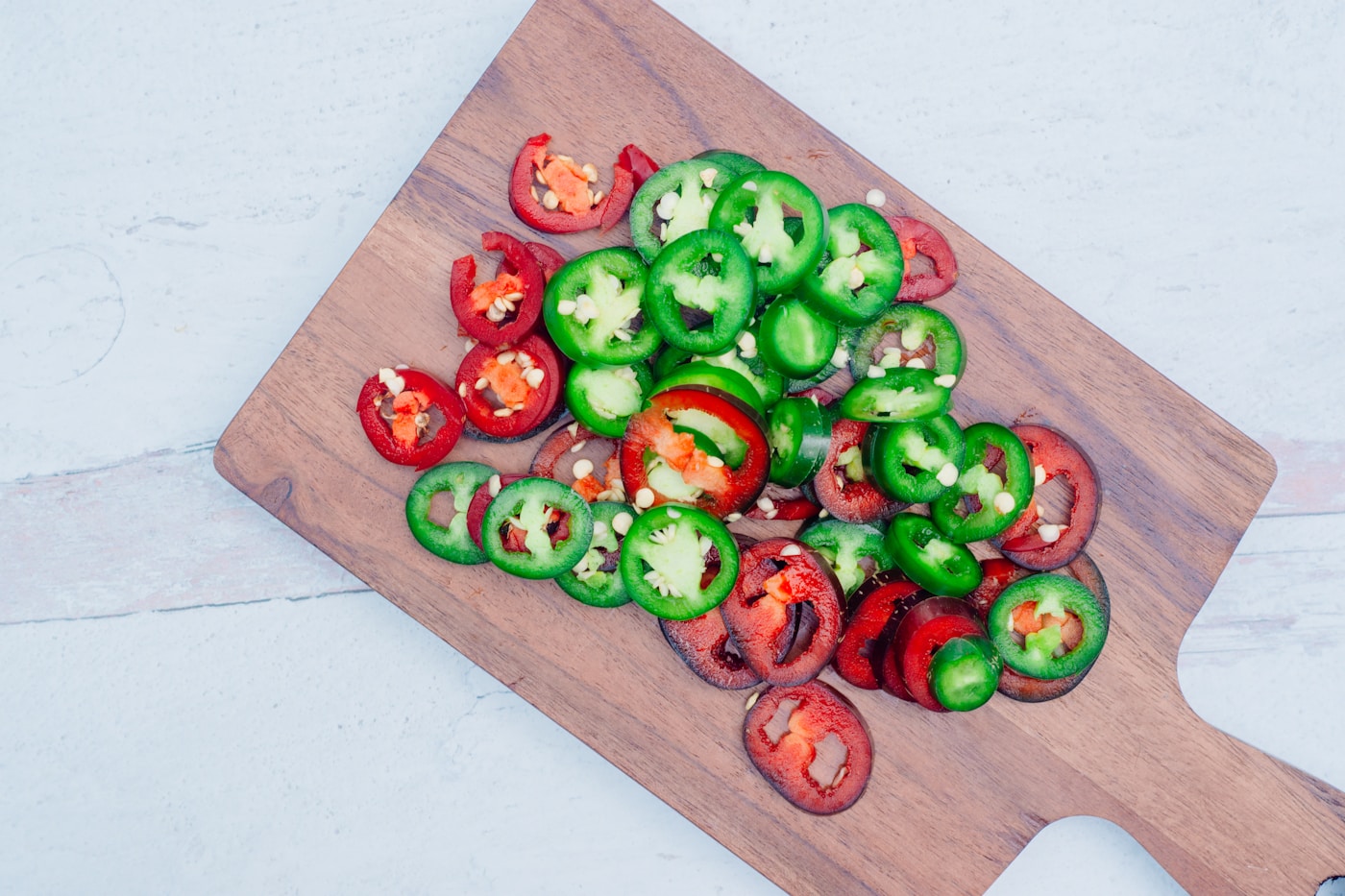 Sliced jalapeno peppers and red chilis on a wooden cutting board