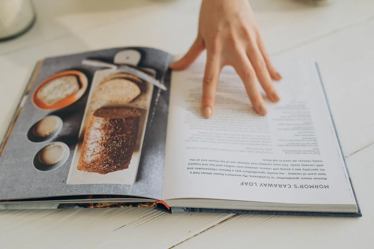 Hand resting on an open cookbook page on a counter