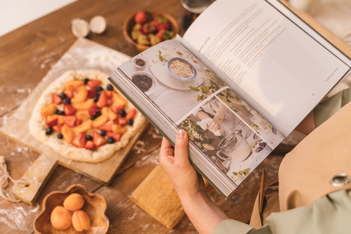 Person reading a cookbook while preparing food