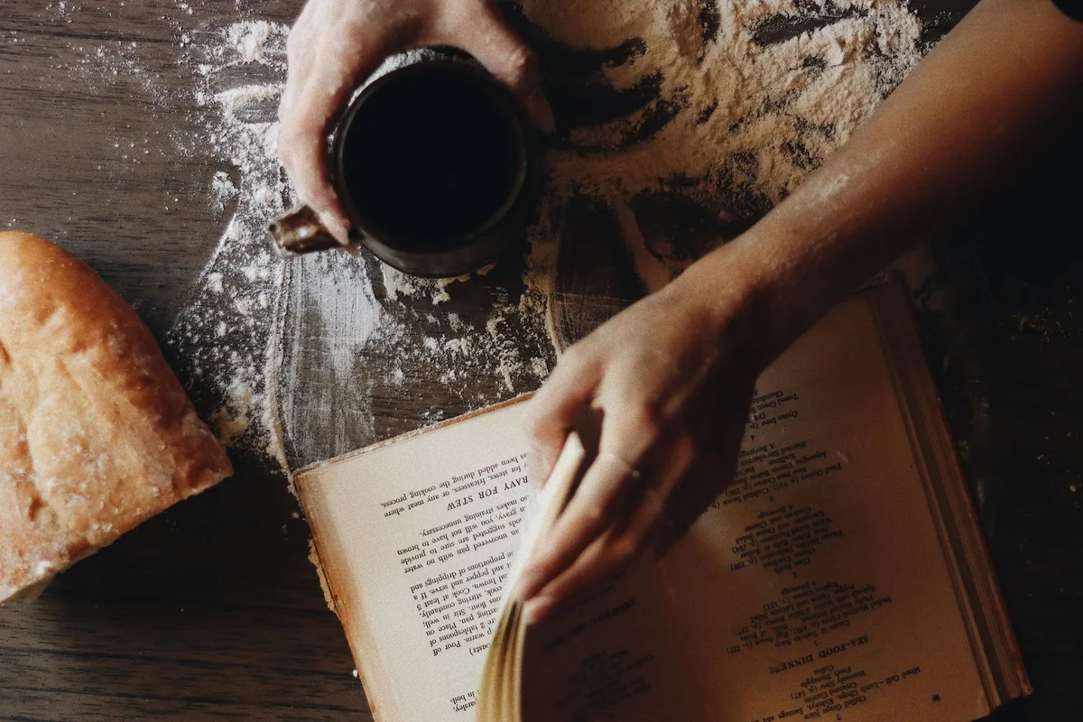 Recipe book on a flour-dusted table with a coffee cup