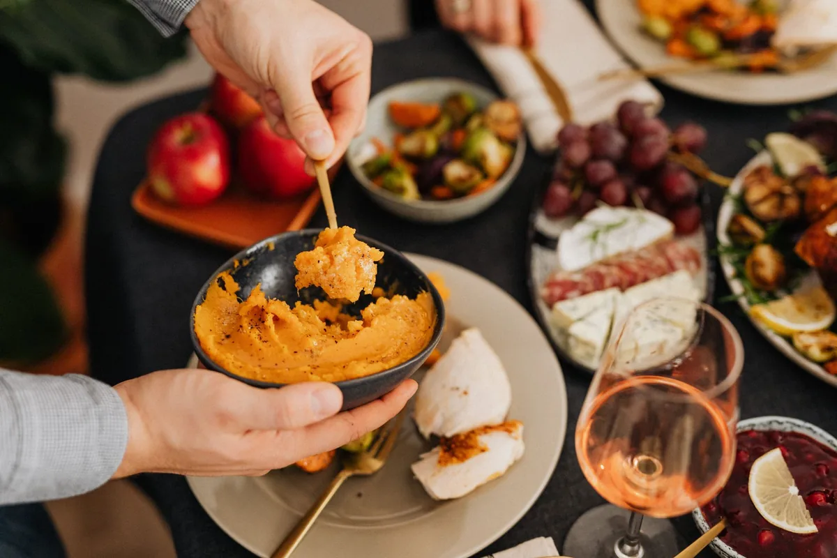 Hands serving mashed potatoes from a bowl at a festive table