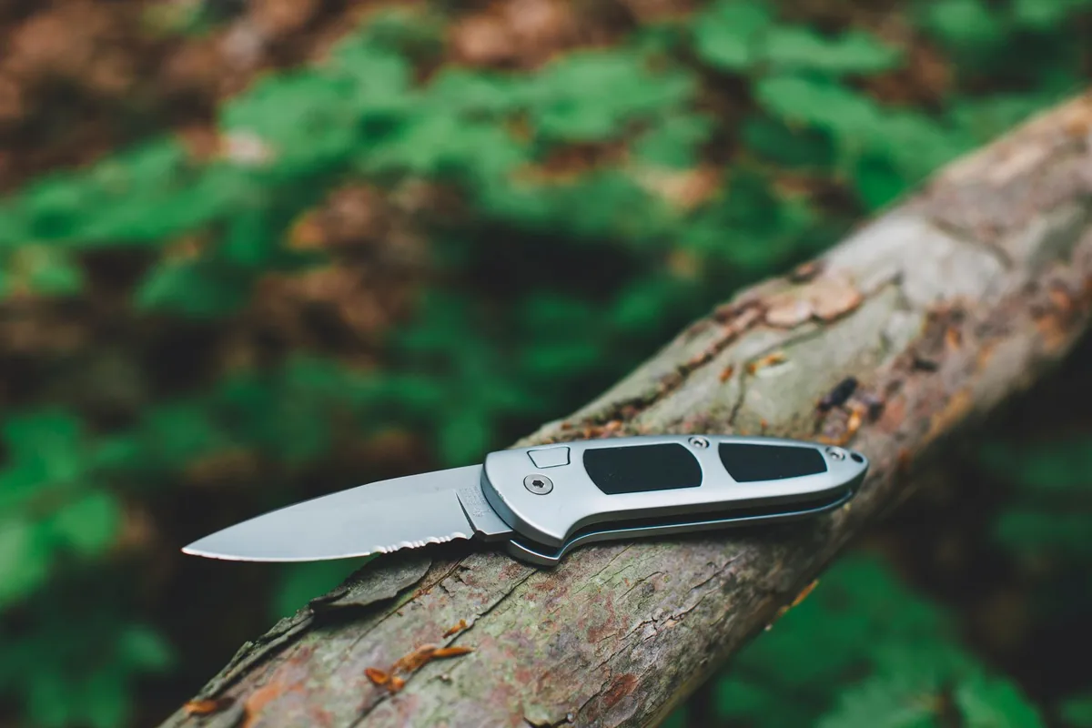 A stainless pocket knife resting on a wooden log