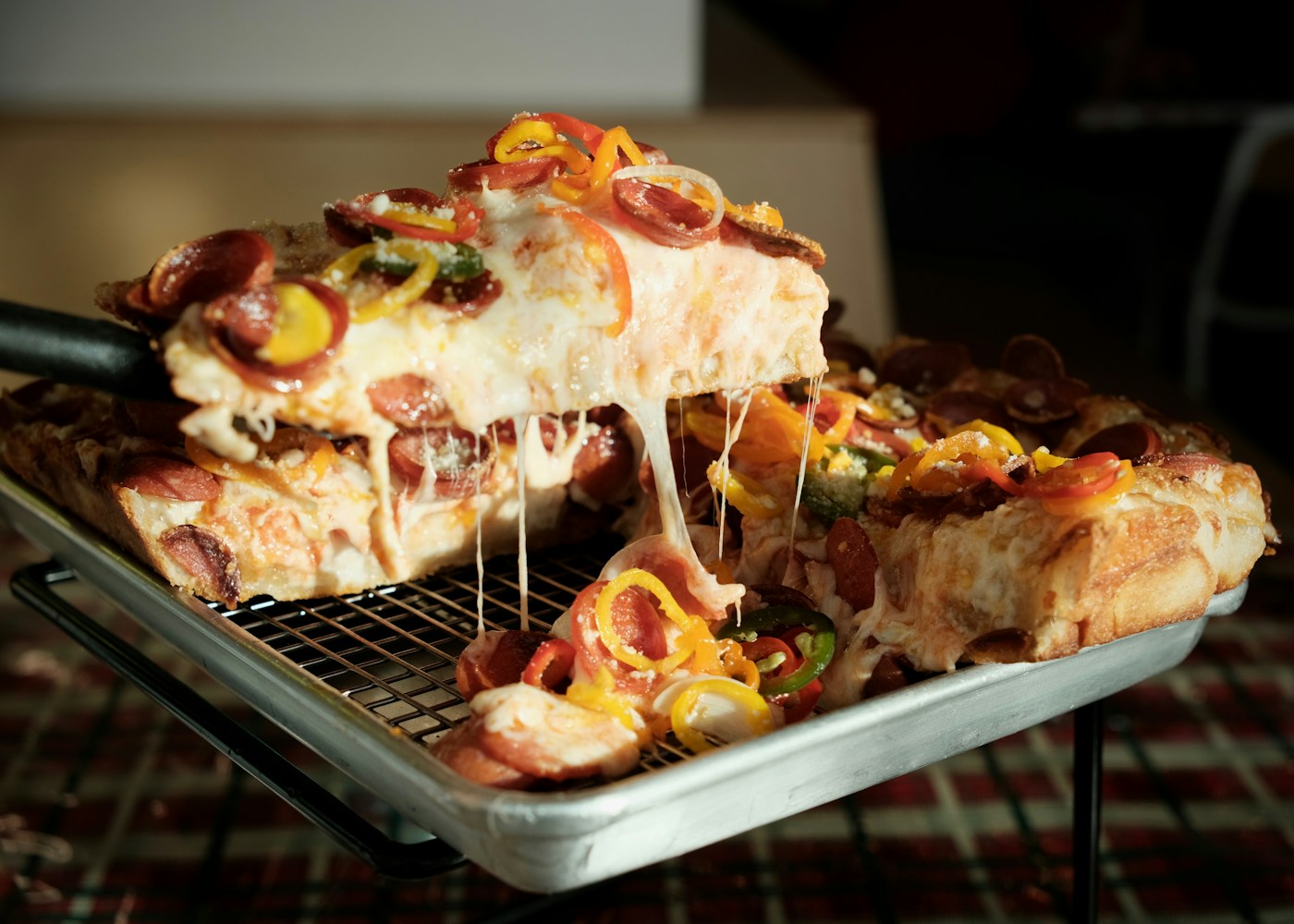 Thick deep dish pizza slice with melted cheese being lifted from the pan