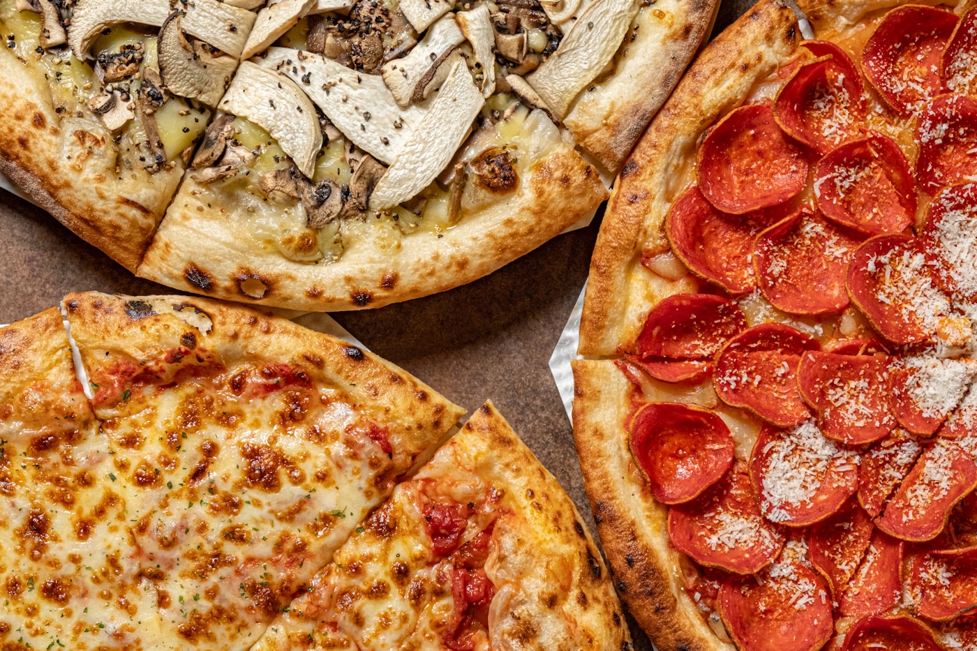 Three different pizzas side by side: mushroom and chicken white pizza, cheese, and pepperoni