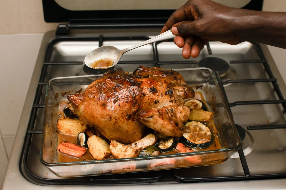 Baked chicken with roasted vegetables being basted