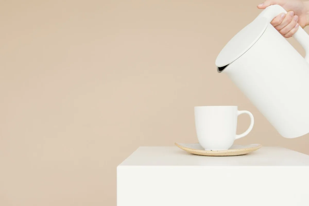A white kettle pouring into a matching cup