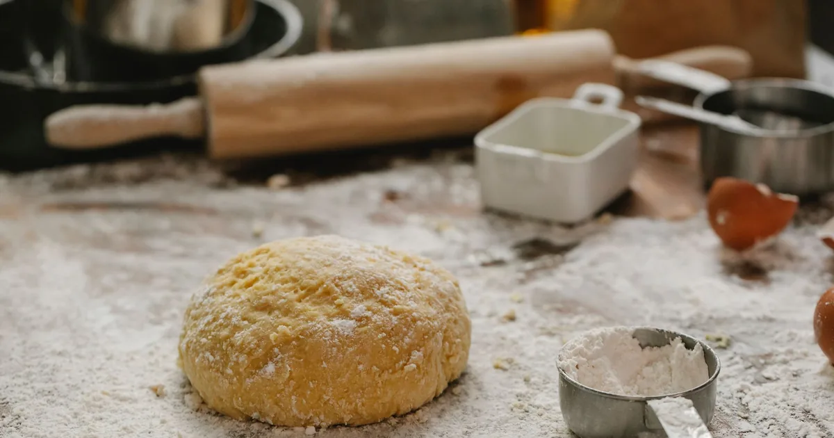 A ball of dough beside a rolling pin and a measuring cup