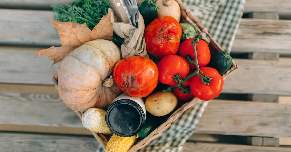 A basket of tomatoes, squash and greens on a wooden table