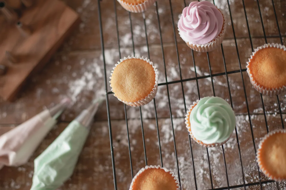 A batch of plain cupcakes in paper cases set out on a wire cooling rack