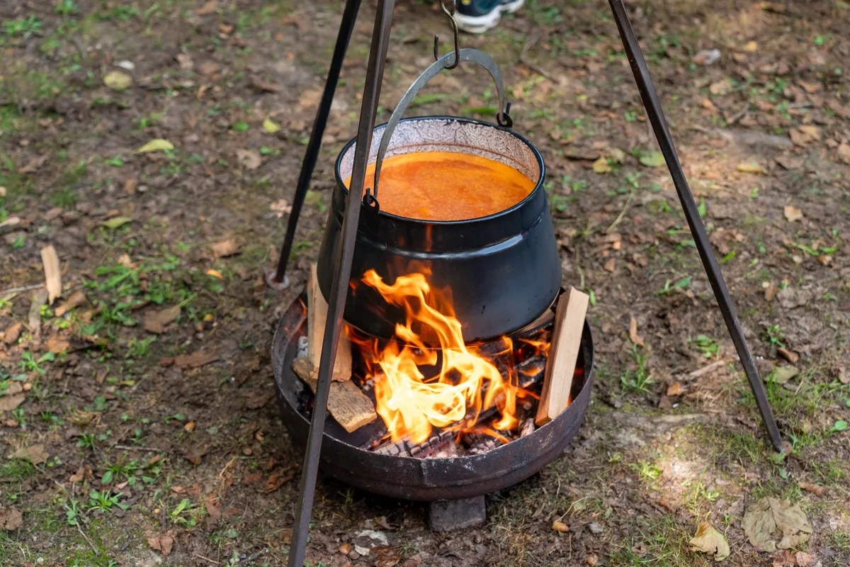 A black pot of soup hanging from a tripod over a fire pit