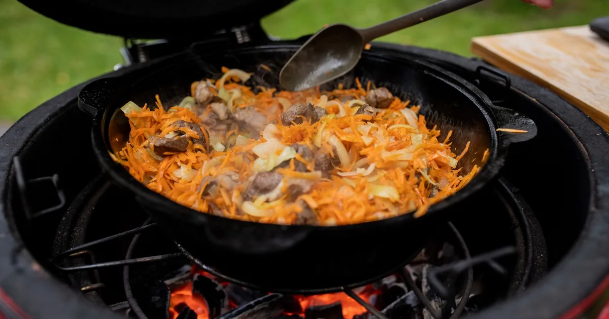 Vegetables and meat cooking in a cast iron pan over a grill