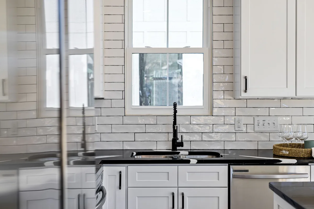 A black faucet over a double sink below a kitchen window