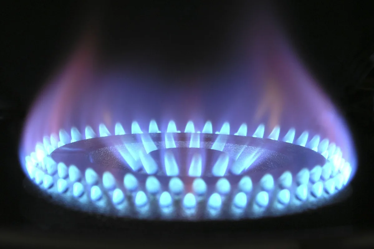 A blue gas flame ring burning on a stovetop burner beneath a black metal grate
