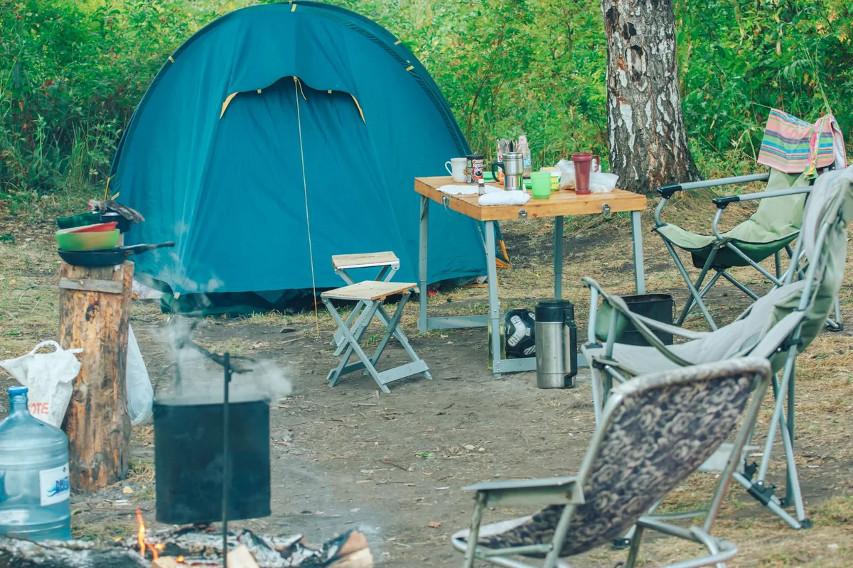 A blue tent and camp chairs at a sunny woodland campsite