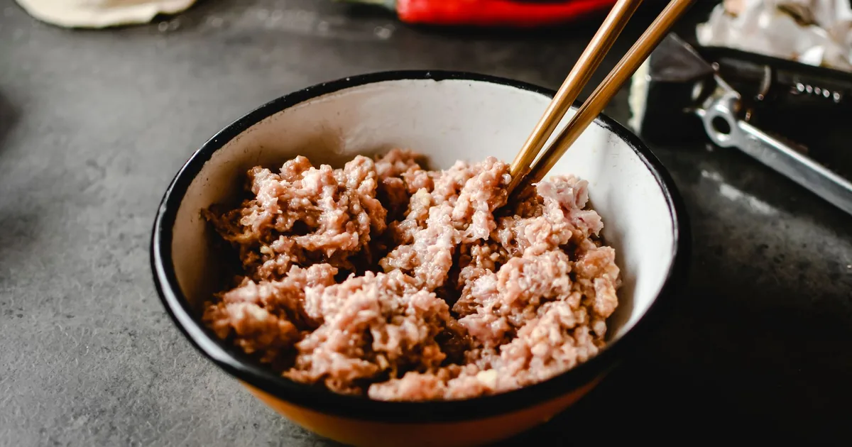 A bowl of freshly ground red meat on a light wooden worktop beside a small dish of salt