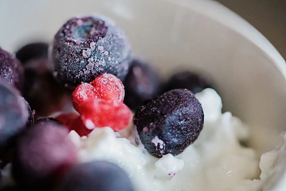 A bowl of frozen mixed berries and mango chunks with a light frost on them